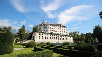 Ein großes, historisches Gebäude mit mehreren Stockwerken und einem zentralen Turm, umgeben von gepflegten Gärten und einer Bergkulisse.