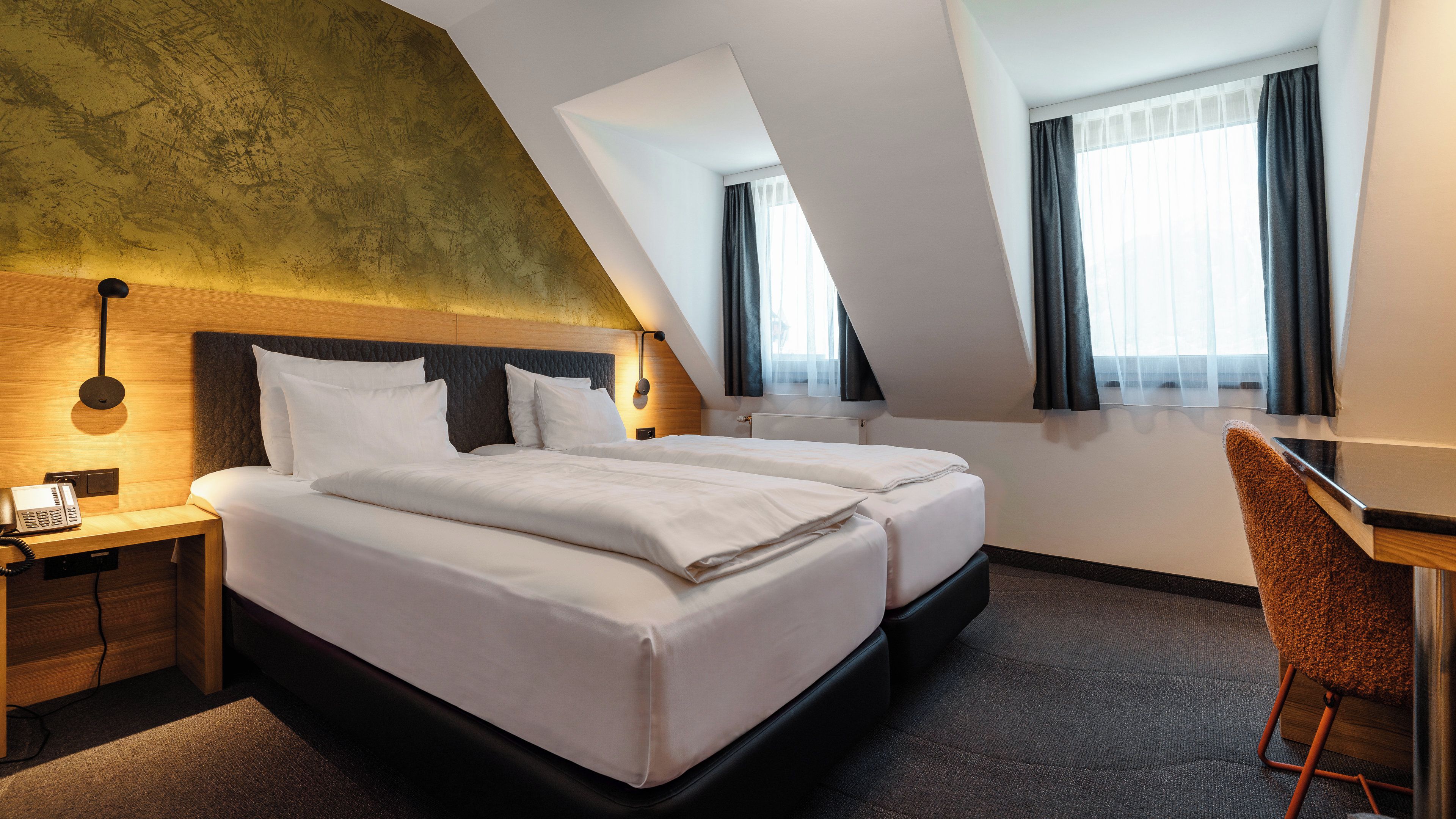 A hotel room with a vaulted ceiling, two beds, a desk, and a chair.