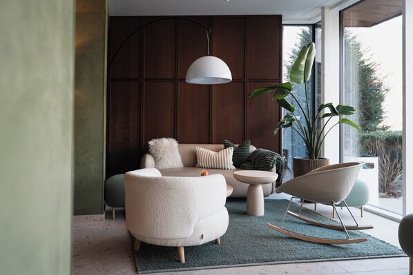 A modern living room with a sofa, a round chair, a hanging light fixture, and a large potted plant.