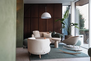 Un salon moderne avec un canapé, un fauteuil rond, un luminaire suspendu et une grande plante en pot.