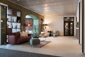A modern lobby with a sofa, chairs, a coffee table, and a bookshelf. - Holiday Inn Innsbruck by IHG (Innsbruck)