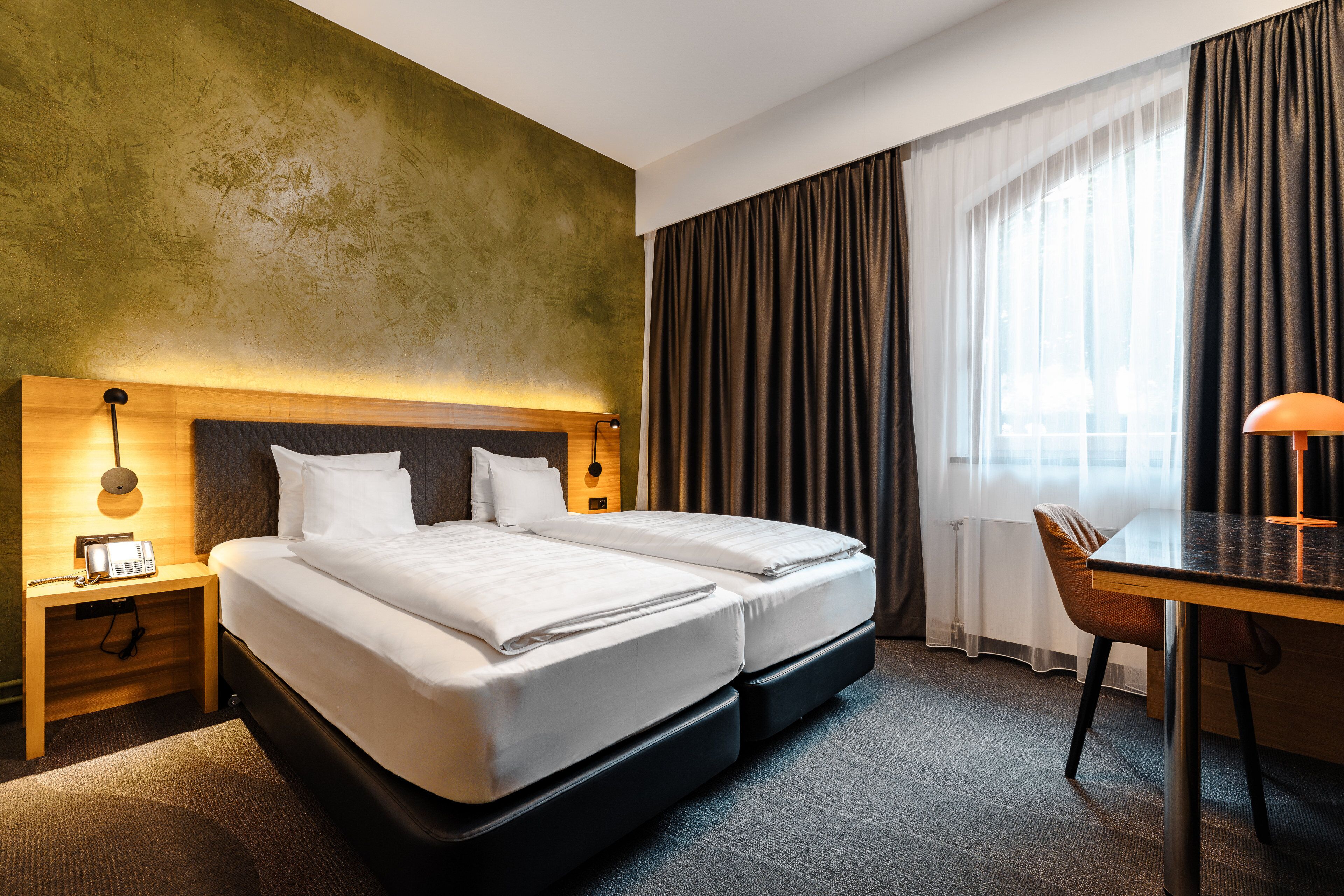 A hotel room with a double bed, a desk, a chair, a telephone, and a lamp.