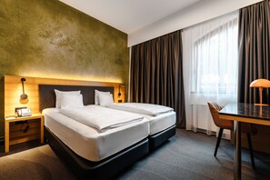 A hotel room with a double bed, a desk, a chair, a telephone, and a lamp.