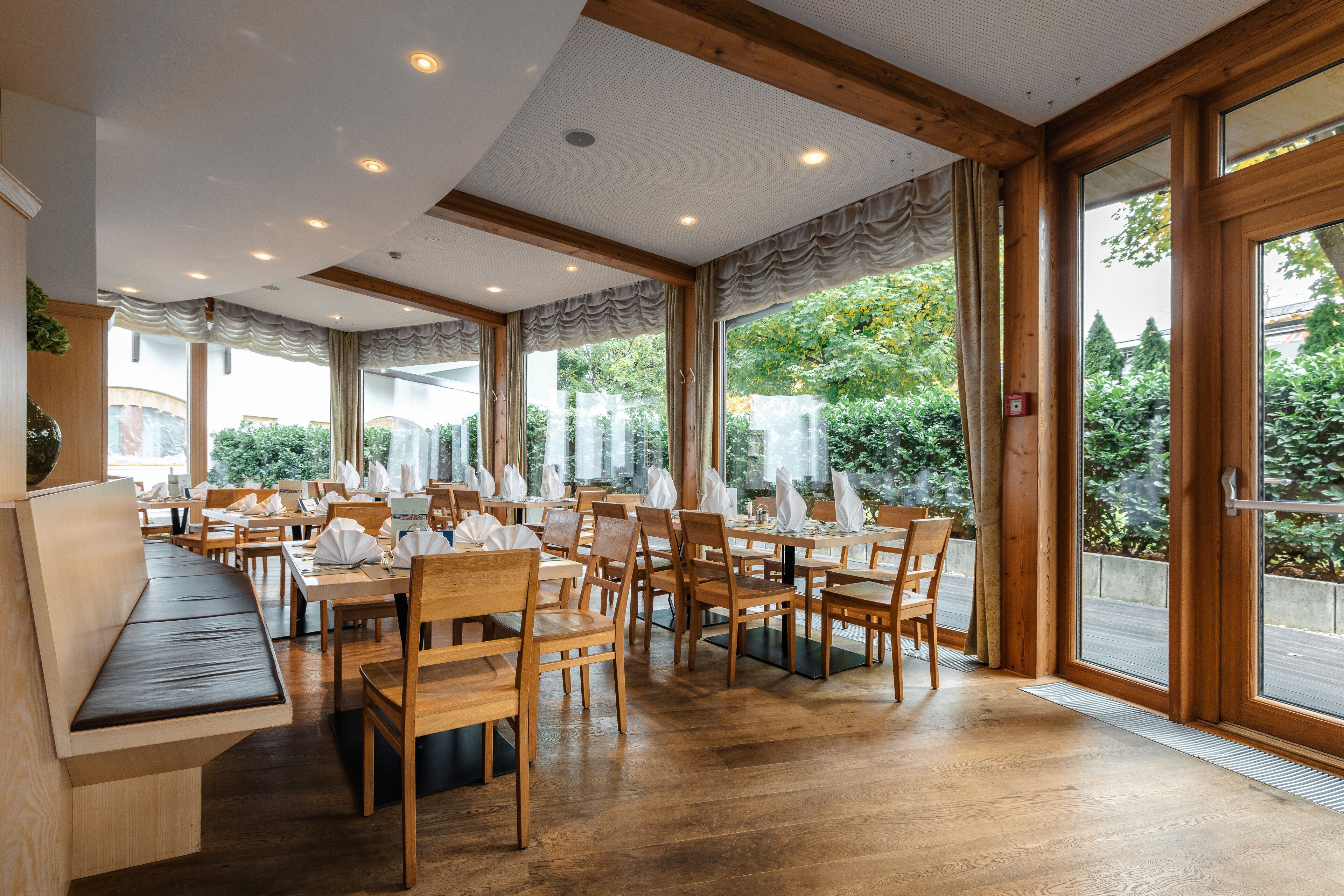 A restaurant with wooden furniture, large windows, and a ceiling with recessed lighting.