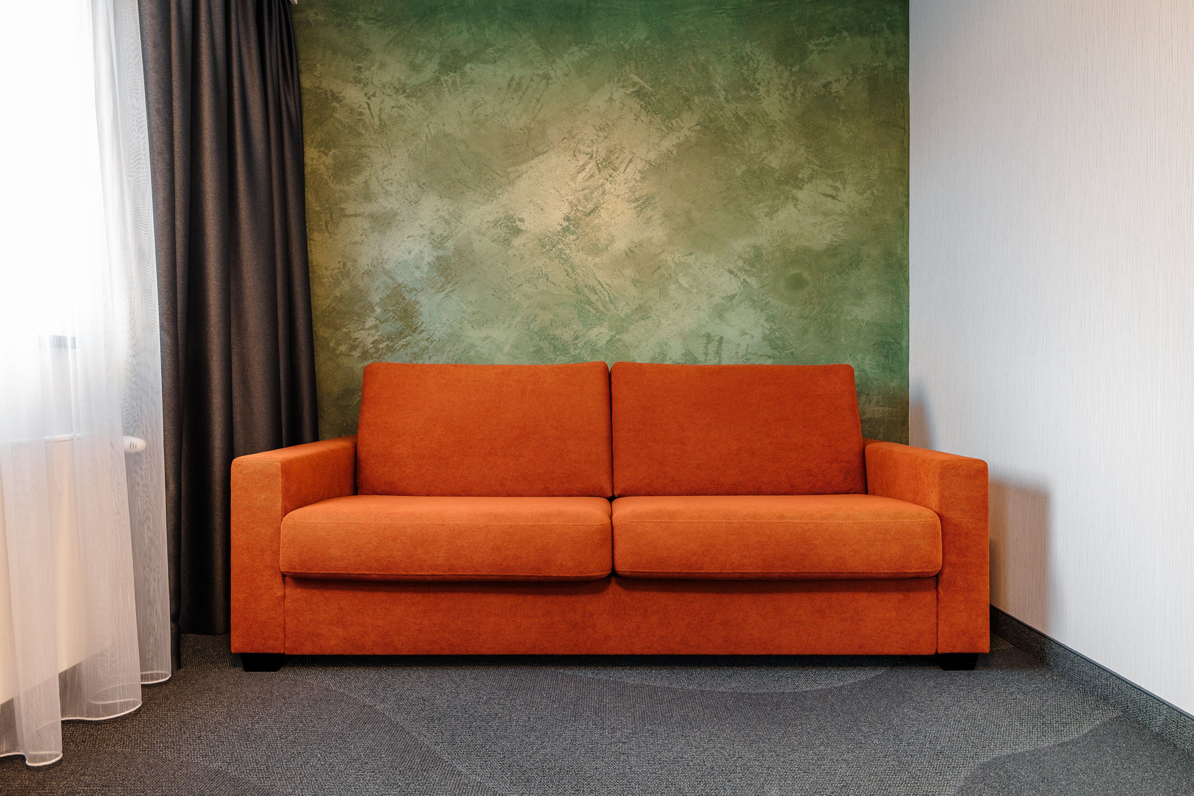 Une pièce avec un mur vert à texture, une moquette grise et un canapé orange.