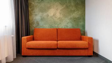 Une pièce avec un mur vert à texture, une moquette grise et un canapé orange.