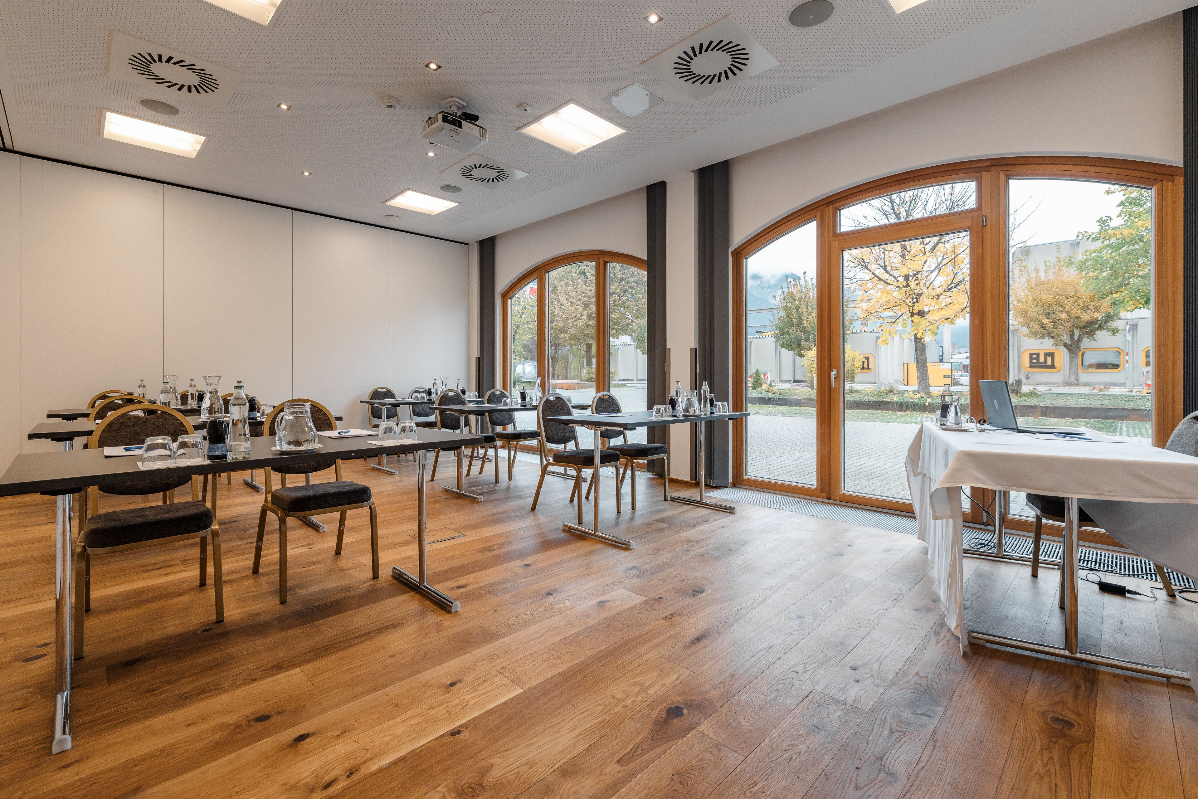 Ein Konferenzraum mit Tischen, Stühlen und einem großen Fenster mit Blick auf Bäume und Gebäude.