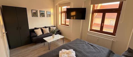 A hotel room with a bed, a sofa, a TV, and a window with a view.