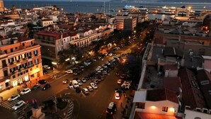Un paisaje urbano al anochecer con edificios, una calle concurrida y un puente al fondo.