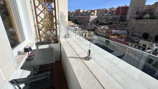 Un balcón con mesa y sillas, una planta en maceta y vistas de un casco antiguo con edificios y un castillo.