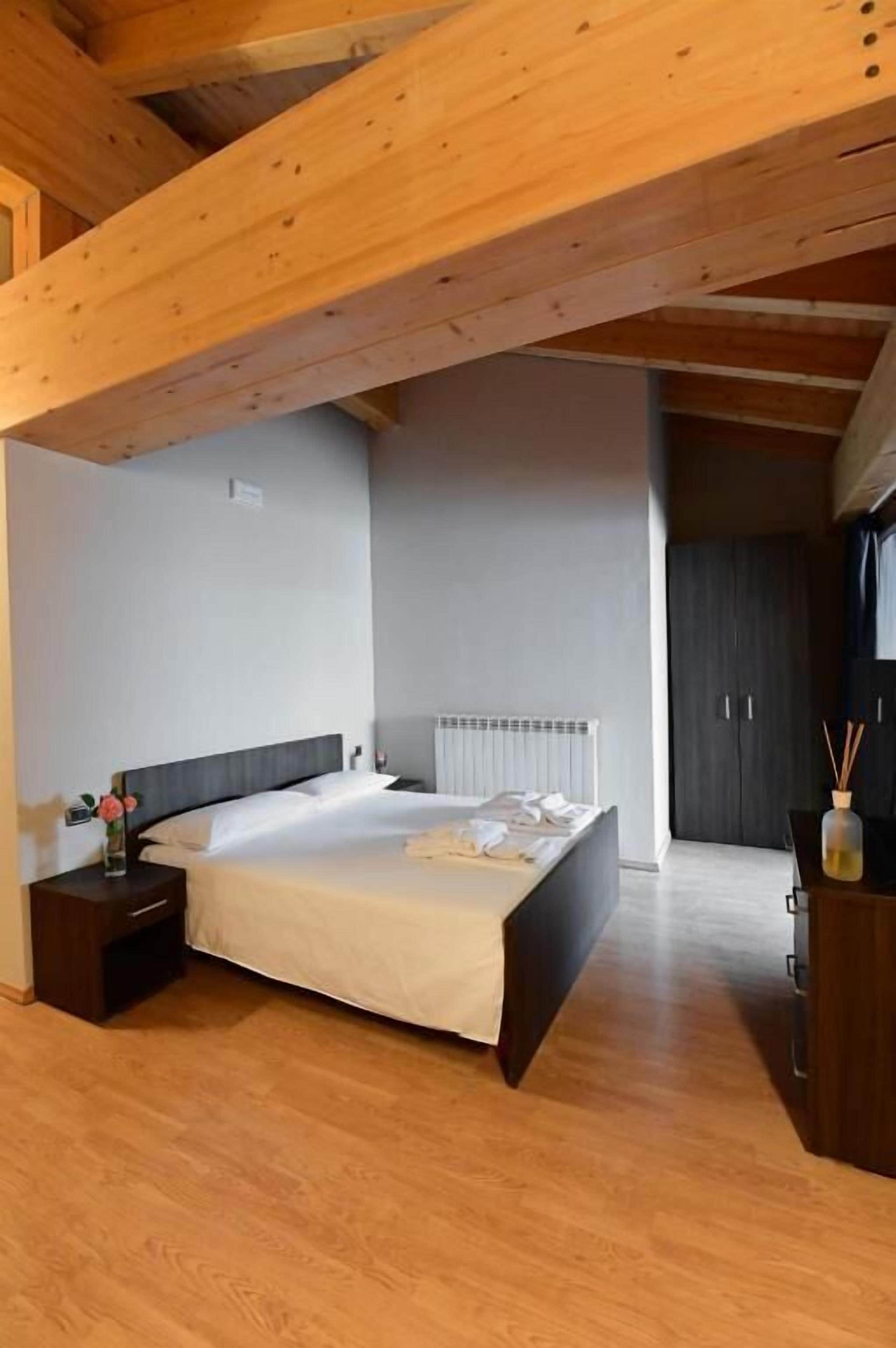 Une chambre avec un plafond en bois, un lit avec du linge de lit blanc, une table de chevet, une commode et un radiateur.
