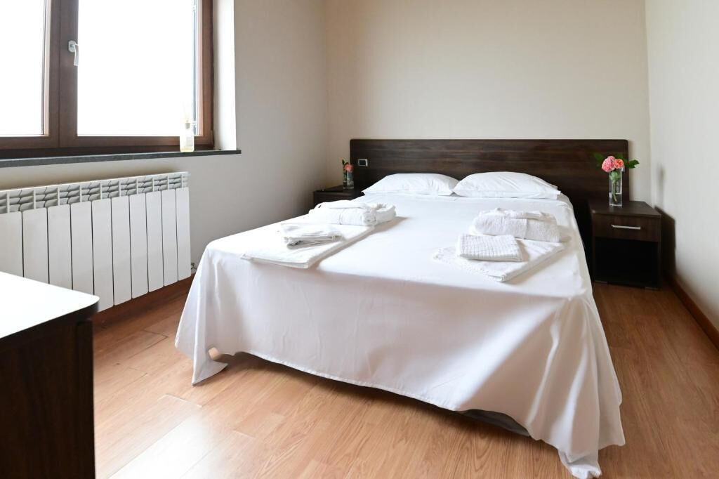 A hotel room with a bed, a bedside table, a nightstand, a radiator, and a window.