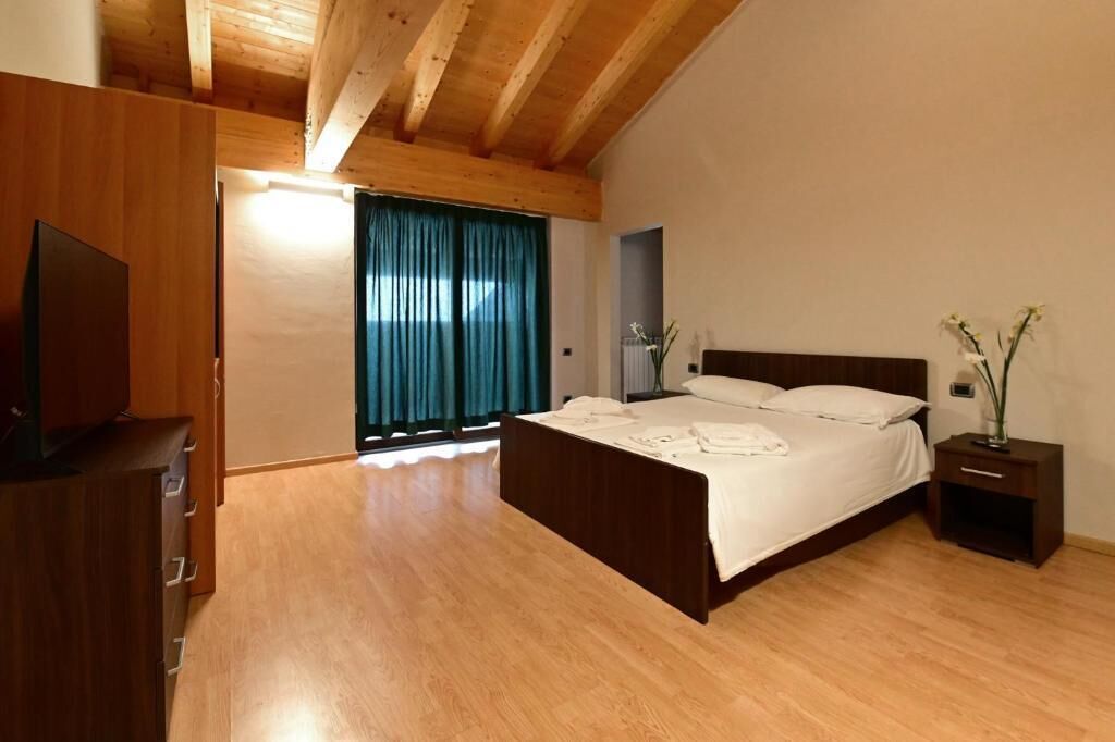 Ein Schlafzimmer mit Holzbalkendecke, einem Bett mit weißen Bettwäsche, einem Nachttisch mit einer Vase und einer Holzkommode.