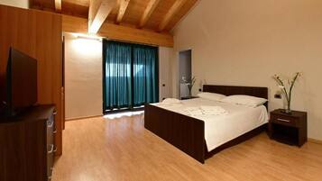 Ein Schlafzimmer mit Holzbalkendecke, einem Bett mit weißen Bettwäsche, einem Nachttisch mit einer Vase und einer Holzkommode.