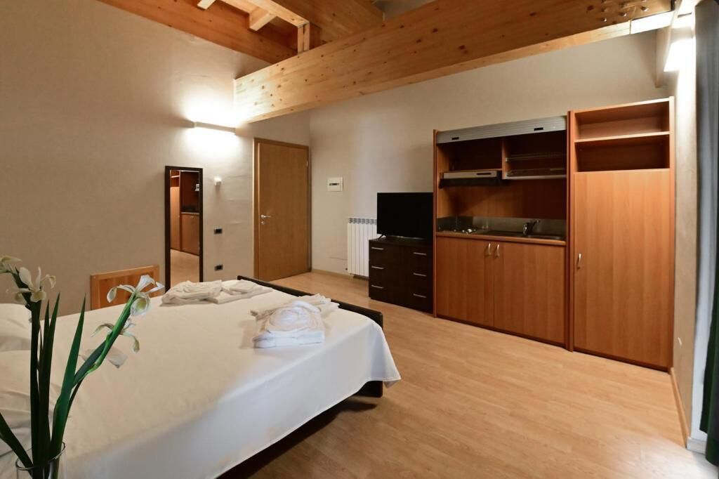 Quarto de hotel com cama, televisão, armários de madeira e banheiro.