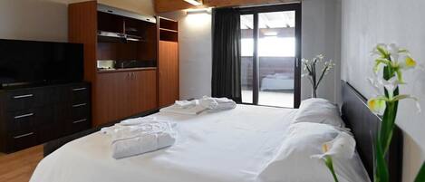A hotel room with a bed, a TV, a wardrobe, and a view of the outdoors.
