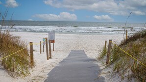 Ein Strandweg, der zum Meer führt, mit einem Rettungsschwimmer-Schild und einem Warnschild.