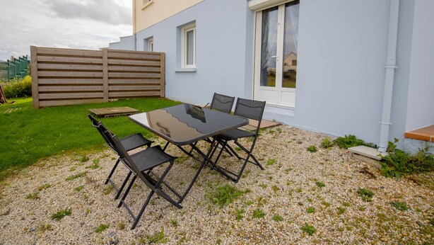 An outdoor seating area with a table and chairs, a wooden fence, and a building with windows. - FAMILY STUDIO (Saint-Côme-de-Fresné)