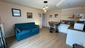 A compact living space with a sofa, a dining area, and a kitchenette. - FAMILY STUDIO (Saint-Côme-de-Fresné)