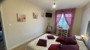 A bedroom with a bed, pillows, a desk, a chair, a television, and a window with curtains. - FAMILY STUDIO (Saint-Côme-de-Fresné)