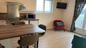 A modern kitchen with a microwave, coffee maker, and a large window. There is a red chair and a teal sofa in the living area. - FAMILY STUDIO (Saint-Côme-de-Fresné)