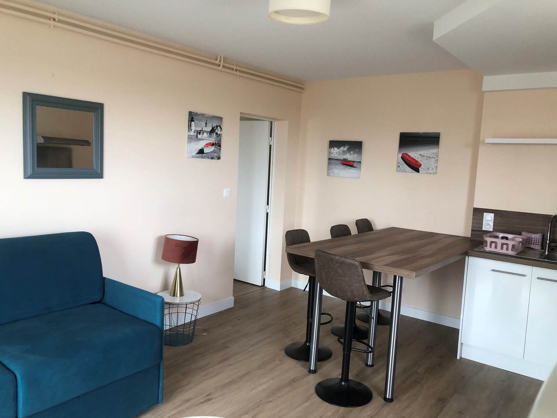 Un salon moderne avec un canapé bleu, une table à manger avec quatre chaises et un coin cuisine doté d’un meuble blanc.
