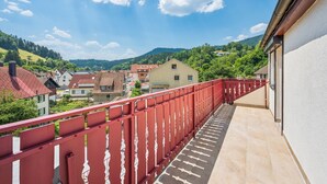Ein Balkon mit roter Brüstung, der auf ein Wohngebiet mit Häusern und einer Hügelkulisse blickt.