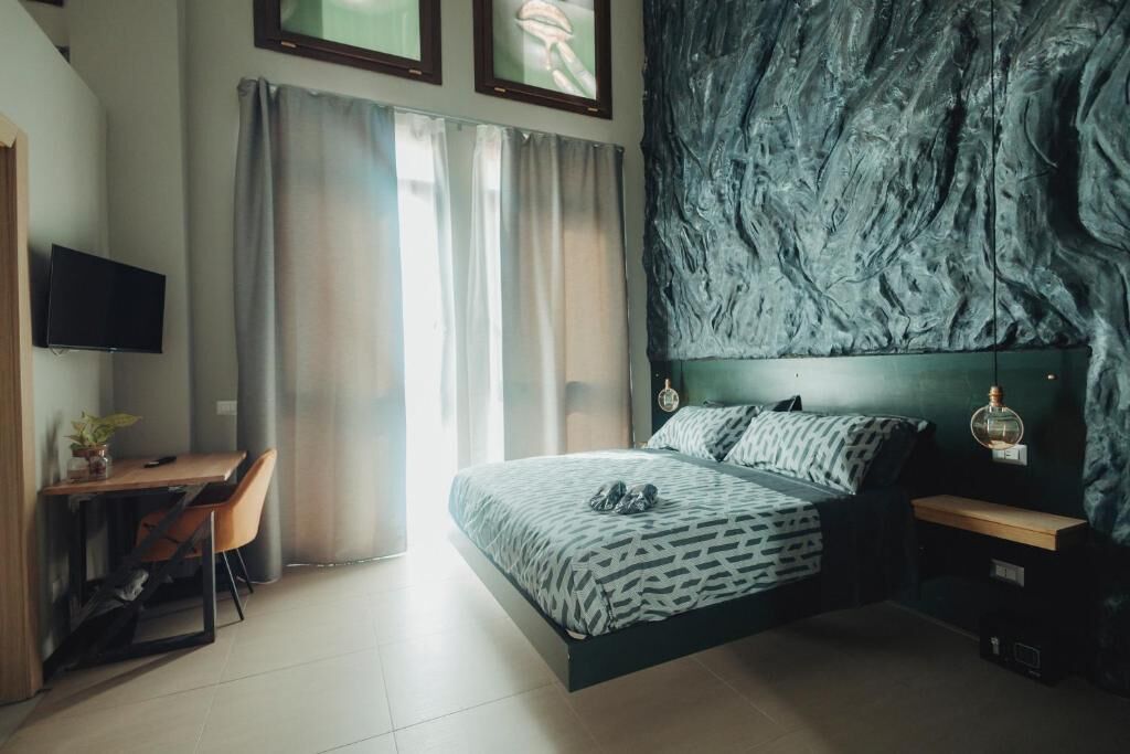 A bedroom with a bed, a desk, a chair, a TV, and a wall with a textured pattern.