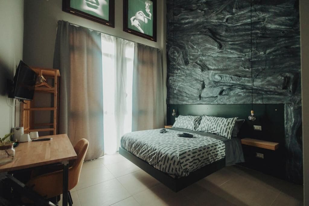 Un dormitorio con cama, escritorio, silla, televisor y un cuadro abstracto grande en la pared.