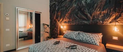 A bedroom with a bed, a mirror, a dark textured wall, and two wall-mounted lights.