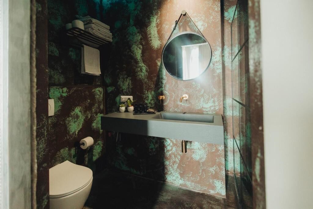 A bathroom with a white toilet, a sink with a mirror above it, and a wall with a greenish, textured pattern.