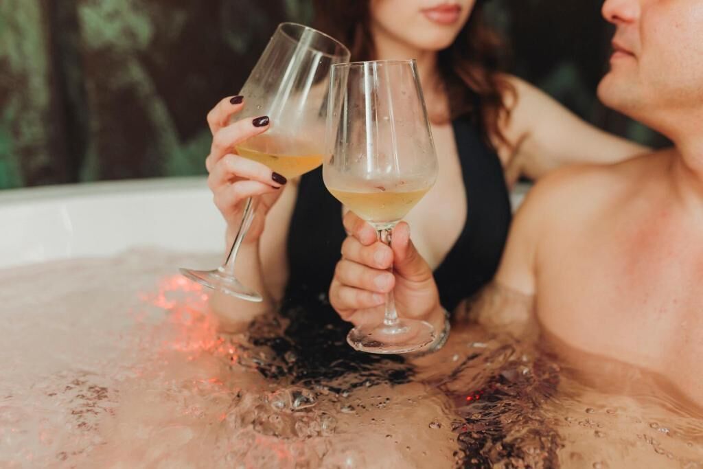 Dos personas en un jacuzzi, disfrutando de bebidas claras.