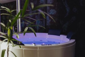 A spa area with a hot tub, a potted plant, and a dark wall with a textured pattern.
