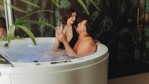 A couple in a hot tub with a plant in the foreground.