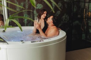 A couple in a hot tub with a plant in the foreground.