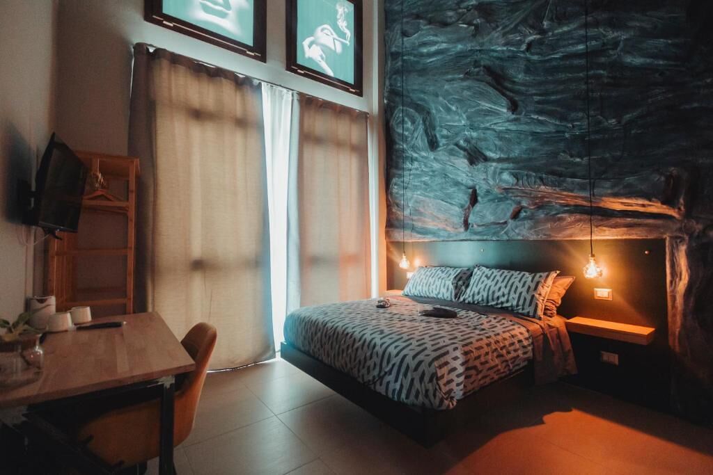 Un dormitorio con cama, escritorio, silla, televisor y una pared con mural texturizado.