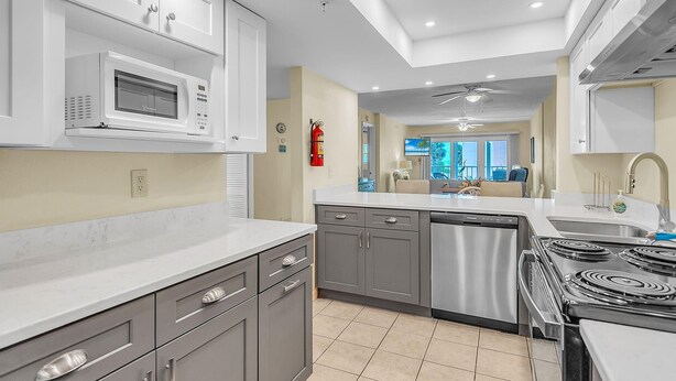 A modern kitchen with a microwave, stove, dishwasher, and grey cabinets. - Shalimar 302 (Indian Rocks Beach)