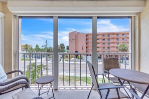 En balkon med fletmøbler, udsigt til en gade og en bygning med teksten 'REEF CLUB 1000'.