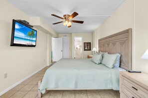 A bedroom with a bed, a ceiling fan, a TV on the wall, and a door leading to another room. - Shalimar 302 (Indian Rocks Beach)