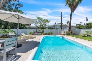 A swimming pool with lounge chairs and an umbrella, surrounded by a fence and greenery. - Shalimar 302 (Indian Rocks Beach)