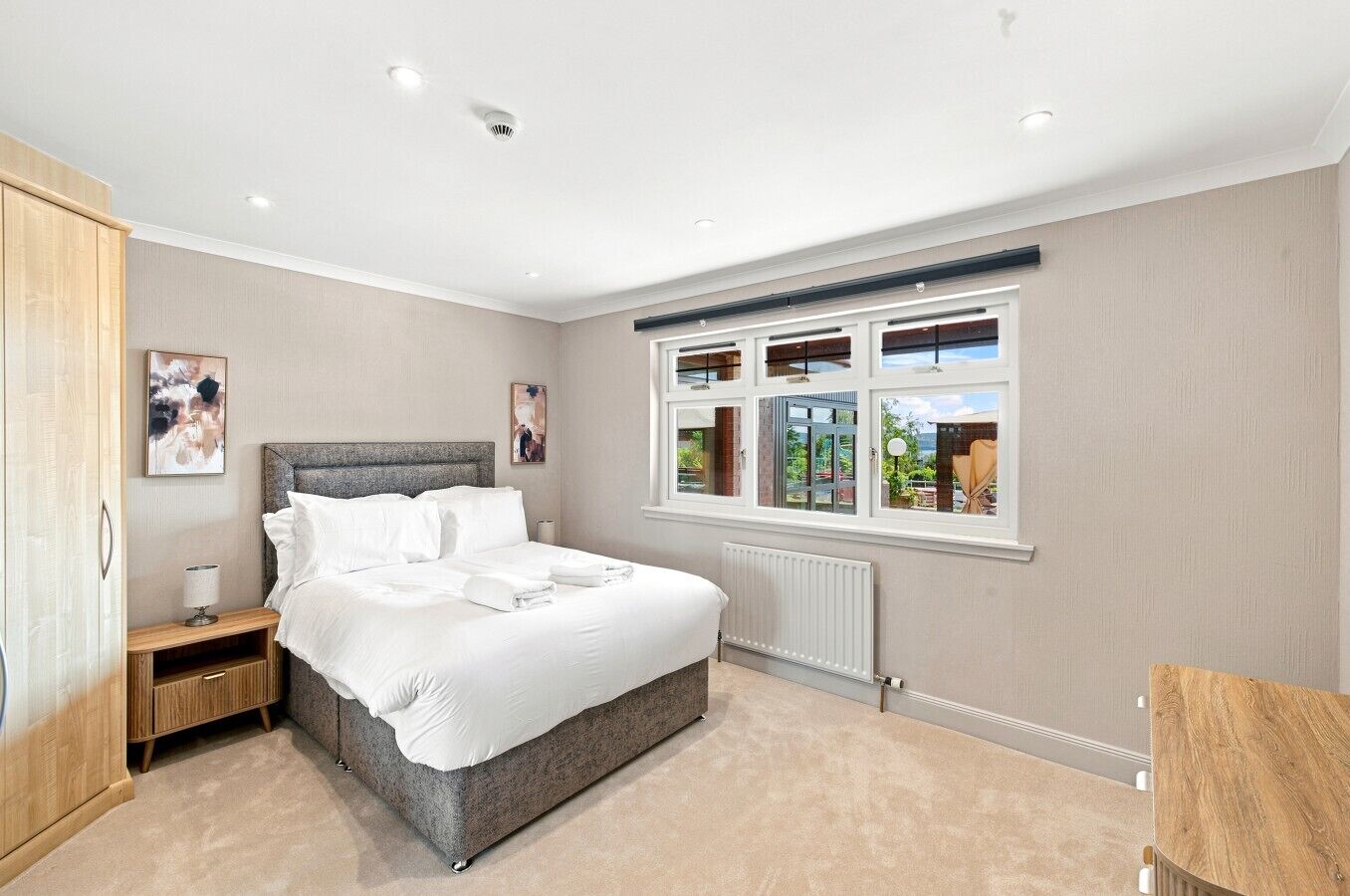 Une chambre à coucher avec un lit, une table de chevet, un radiateur et une fenêtre donnant sur un beau paysage.