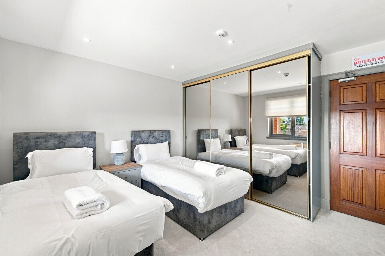 Une chambre d’hôtel avec deux lits, un grand miroir et une porte en bois.