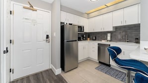 Una cocina moderna con gabinetes blancos, electrodomésticos de acero inoxidable y un taburete azul.