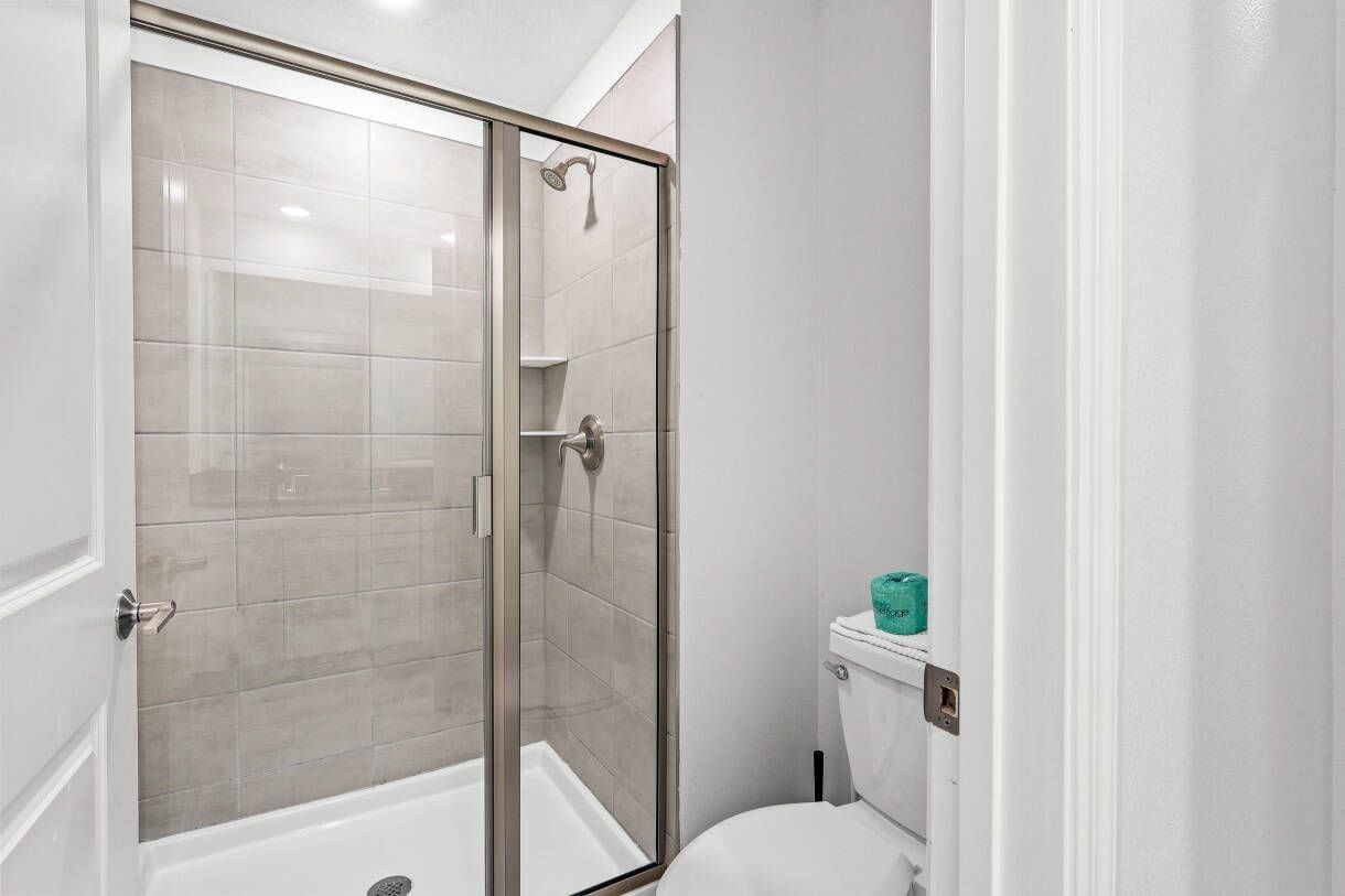 A bathroom with a glass-enclosed shower, a toilet, and a sink.