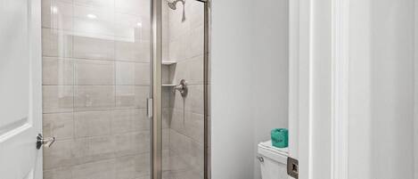 A bathroom with a glass-enclosed shower, a toilet, and a sink.