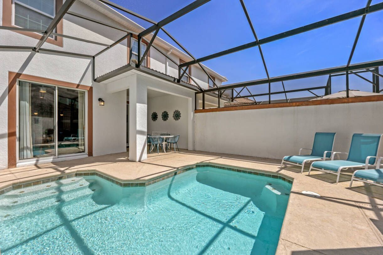 Ein Schwimmbecken mit Liegestühlen, einer überdachten Terrasse und einem Eingang mit Glastür.