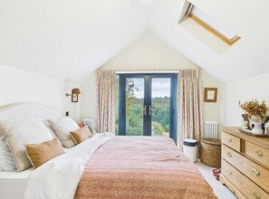 A bedroom with a bed, a dresser, a window with curtains, a radiator, and a skylight. - Cosy 3-bed cottage in sought after village Freshford. Stunning views of valley. (Freshford)