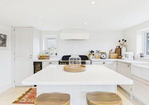 A modern kitchen with white cabinetry, a central island with stools, and a built-in oven. - Cosy 3-bed cottage in sought after village Freshford. Stunning views of valley. (Freshford)