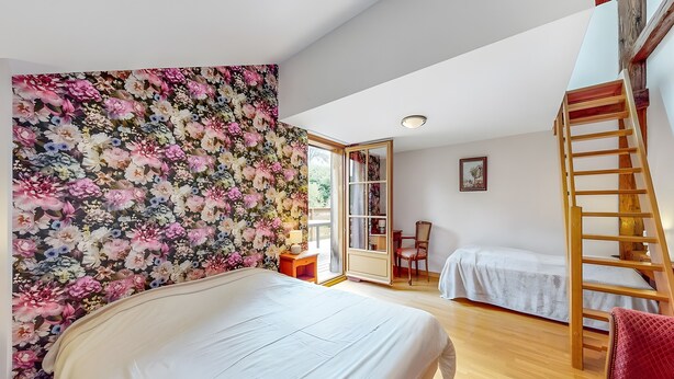 Quarto com uma cama grande, uma escada de madeira, uma cadeira e uma mesa pequena.