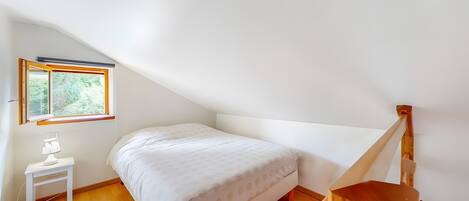 Quarto com uma cama, mesa de cabeceira, abajur, janela e escada de madeira.